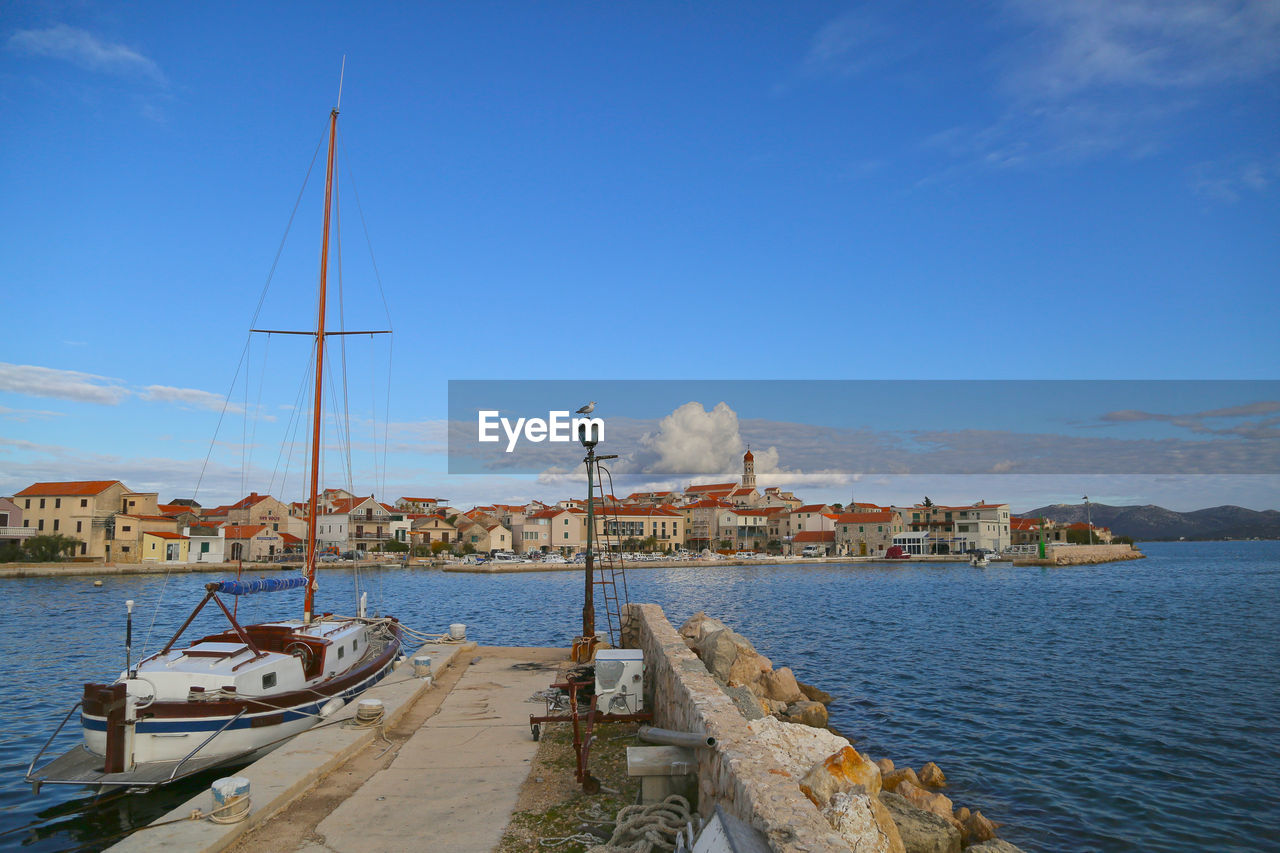 Sailboats moored at harbor by sea against blue sky