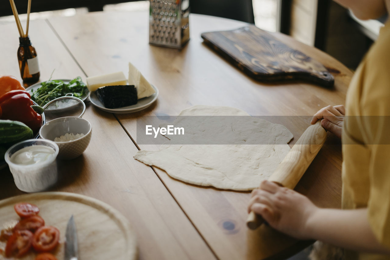 Boy preparing pizza dough with rolling pin on table