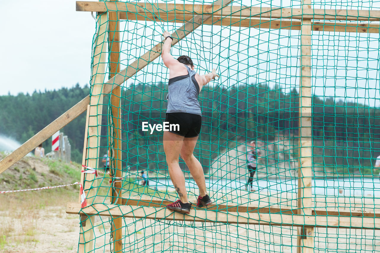 REAR VIEW OF MAN STANDING AGAINST FENCE