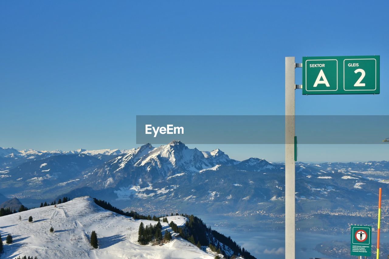 Road sign on snow covered mountain against blue sky