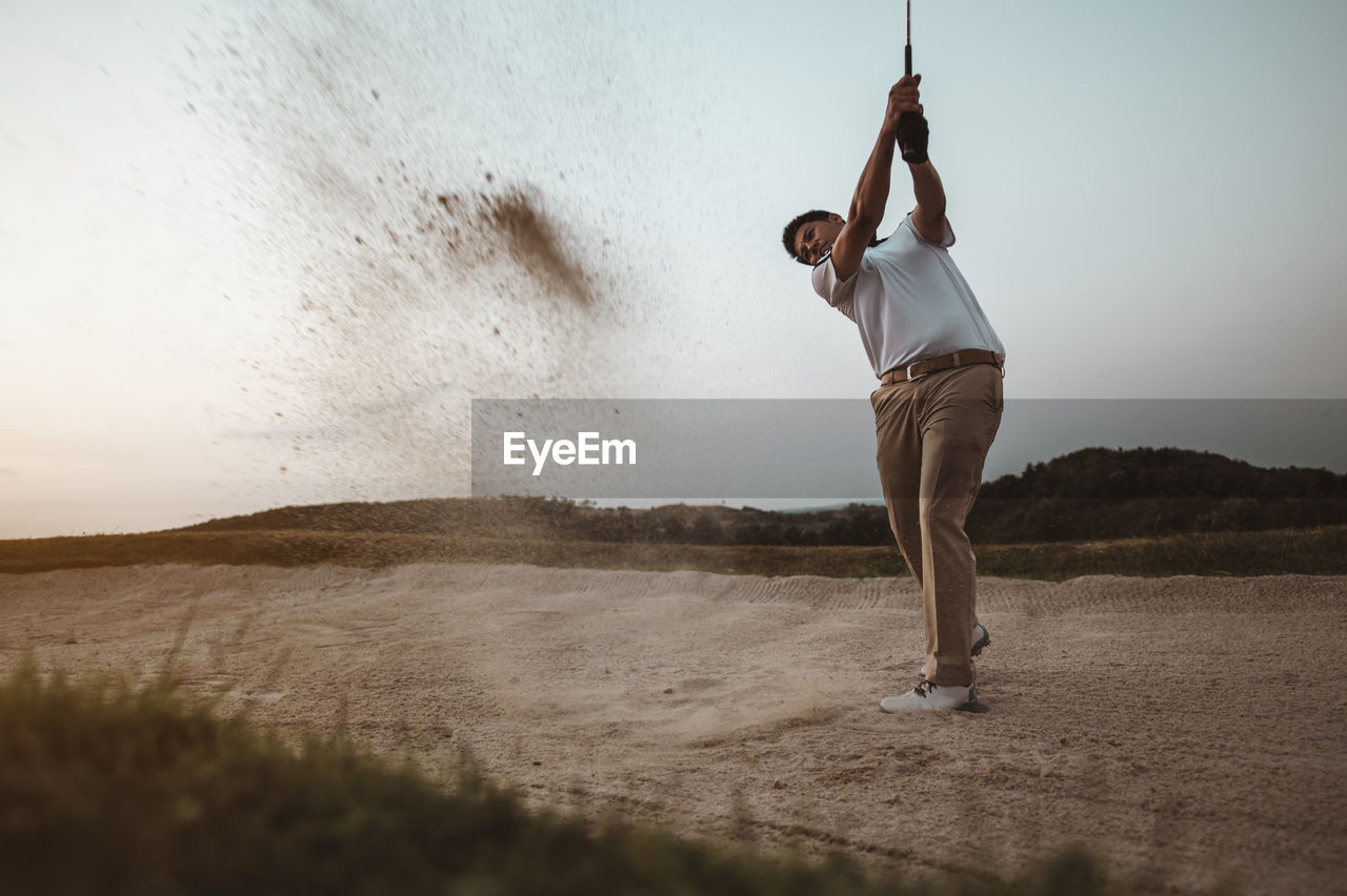 Full length of man playing golf against sky at sunset