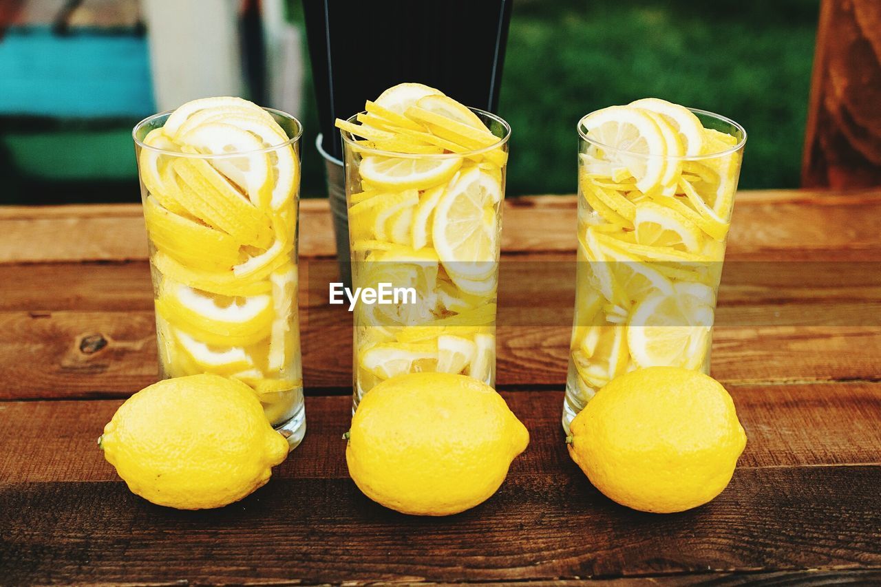 Slices in glasses by lemons on wooden table