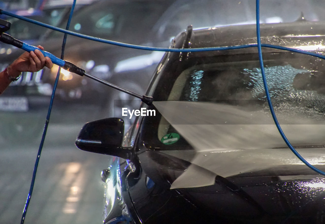 Cropped hand of person spraying water with equipment while cleaning car in garage