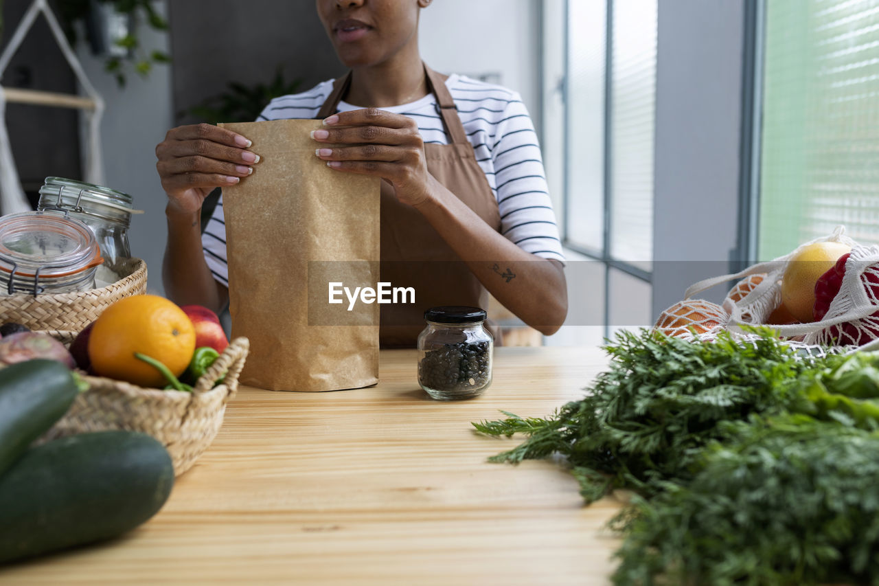 Woman with apron in kitchen , unpacking freshly bought organic fruit and vegetables