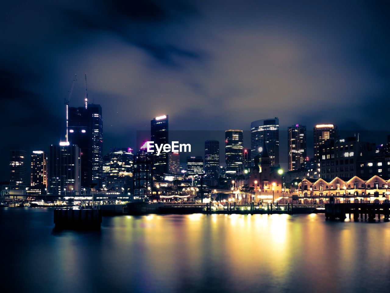 ILLUMINATED BUILDINGS BY RIVER AGAINST SKY IN CITY