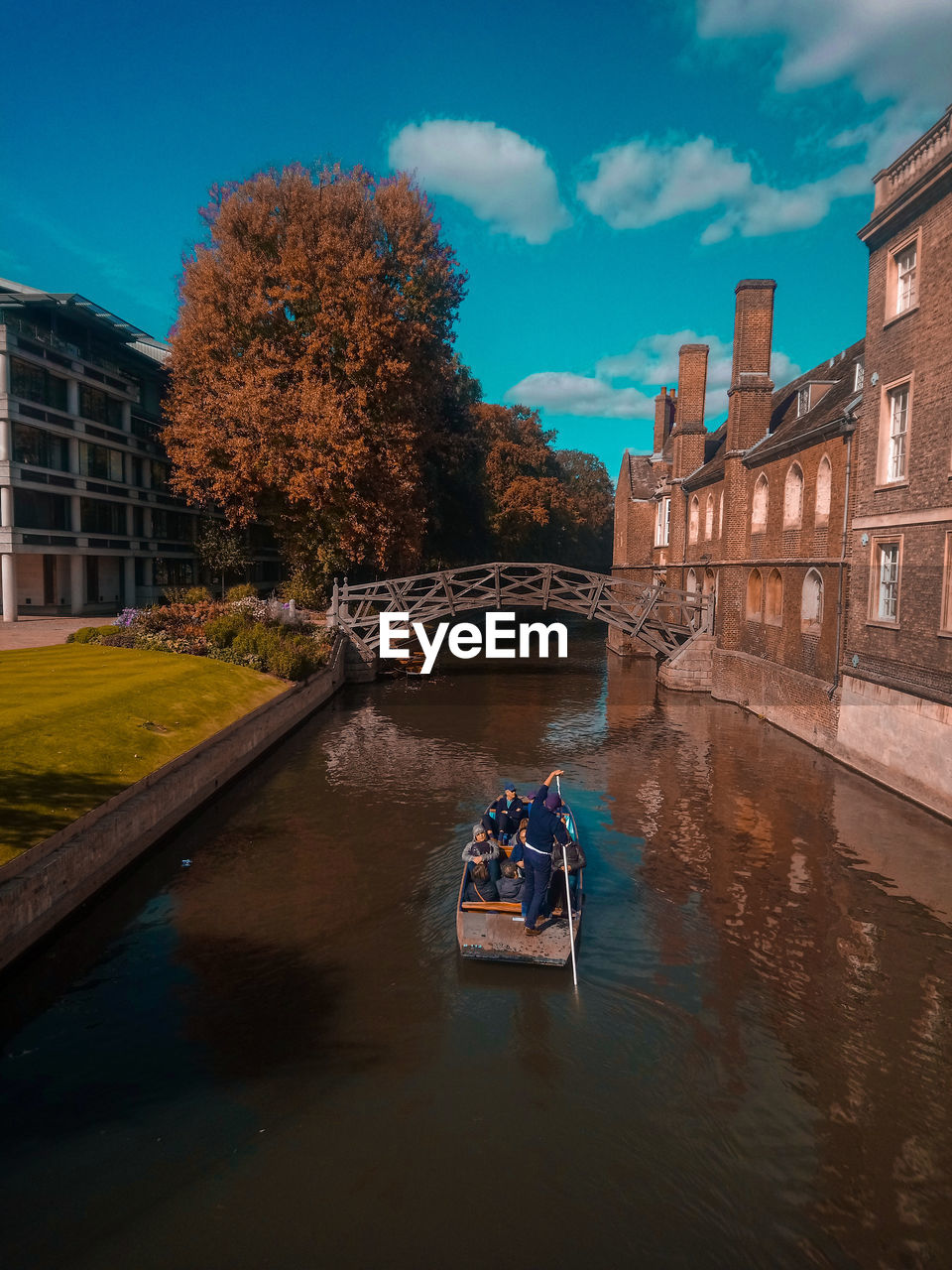 PEOPLE ON RIVER AMIDST BUILDINGS AGAINST SKY