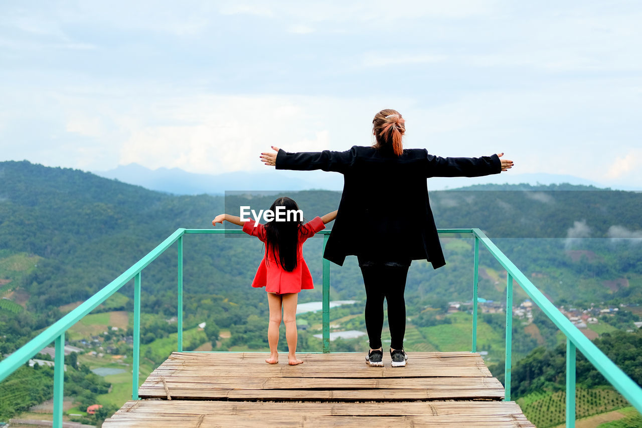 Rear view of mother and daughter with arms outstretched at observation point