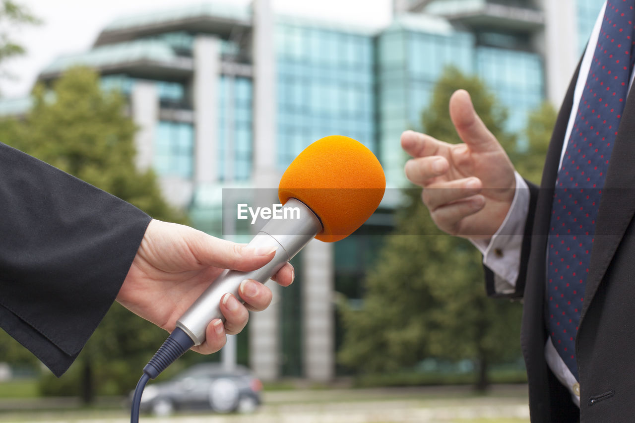 Cropped hand of female journalist with microphone taking interview of male politician