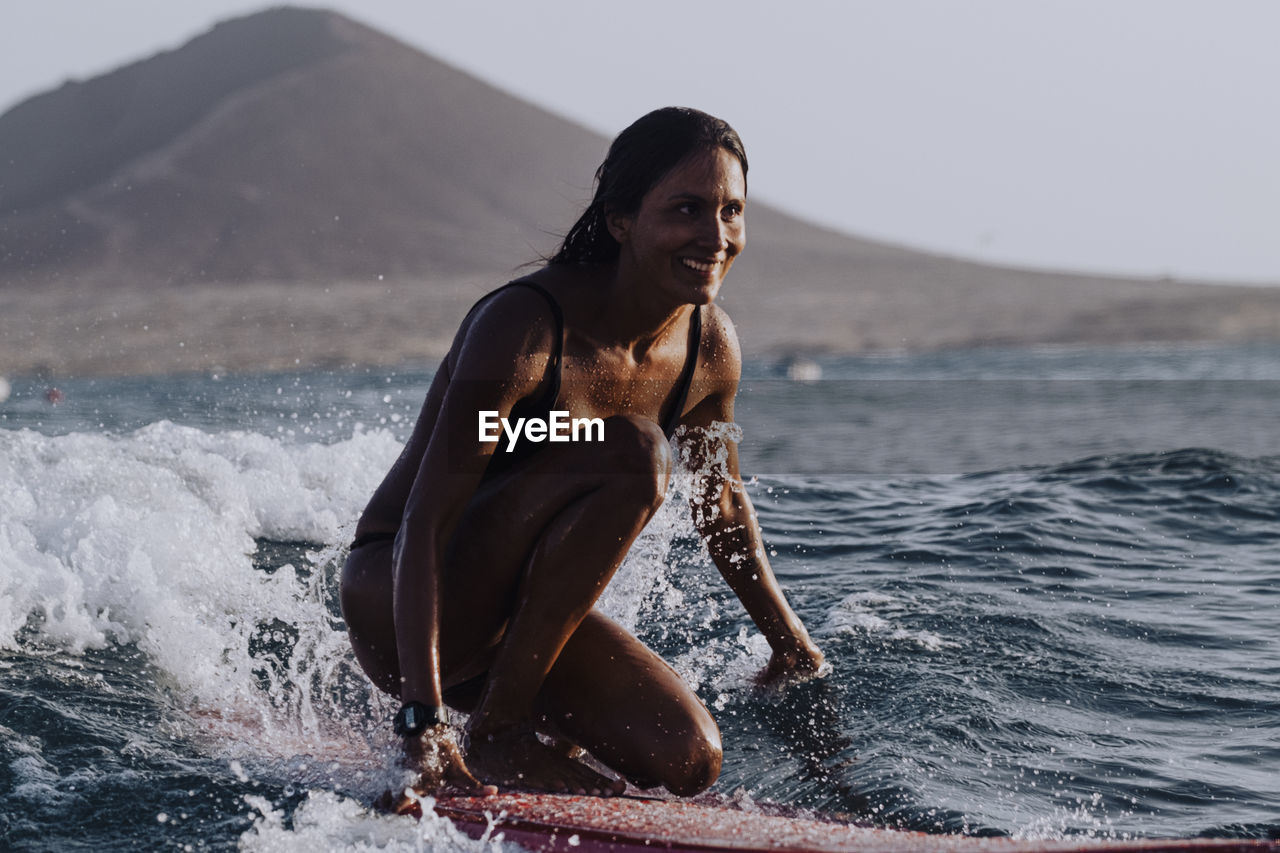 A female surfer smiles while riding a small wave