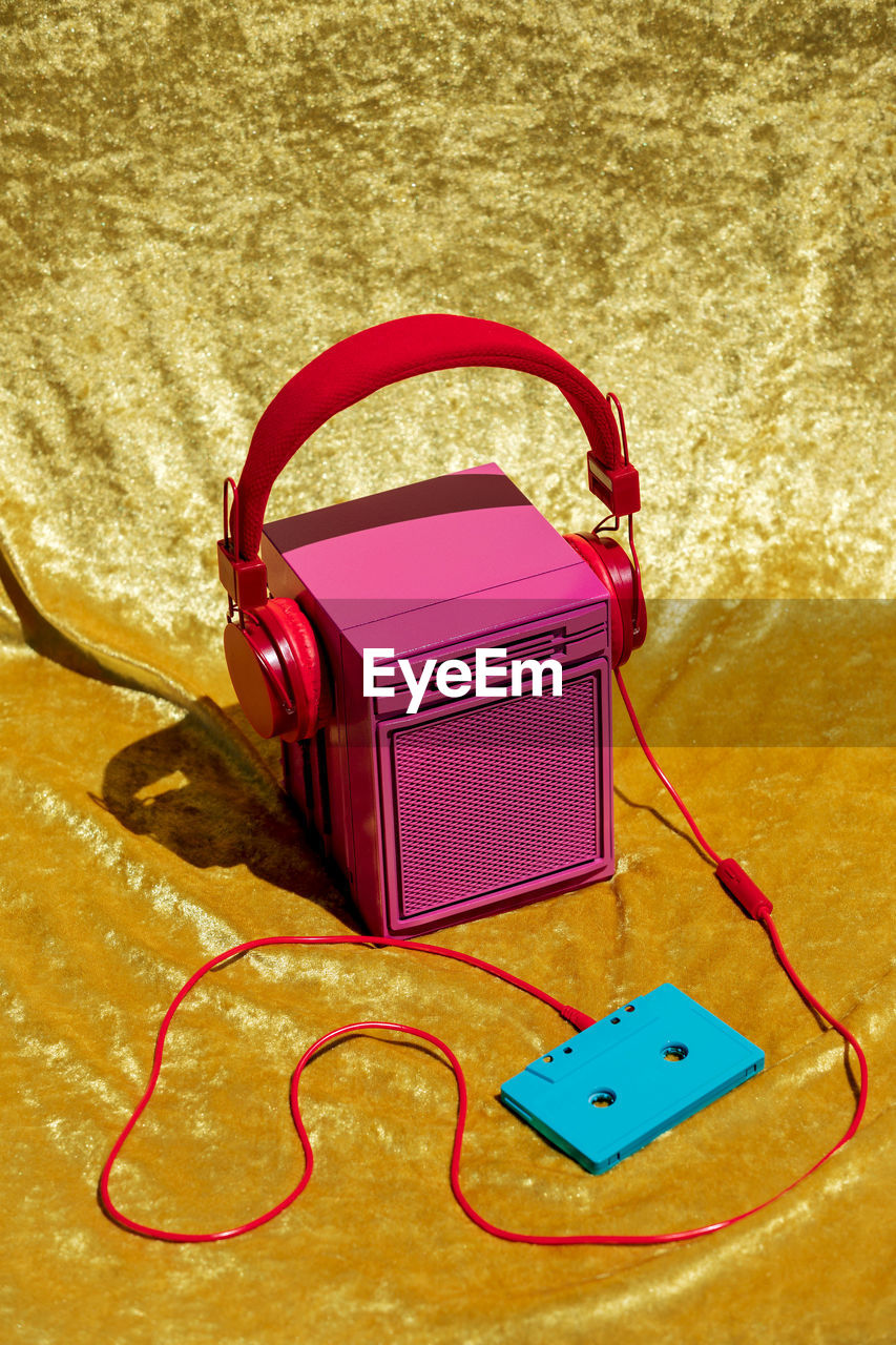 From above of vintage pink stereo speaker in headset connected to audio tape placed on yellow textile in studio