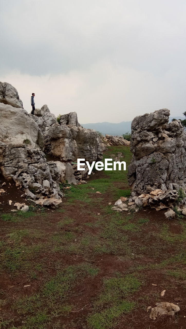 MAN ON ROCK BY LANDSCAPE AGAINST SKY