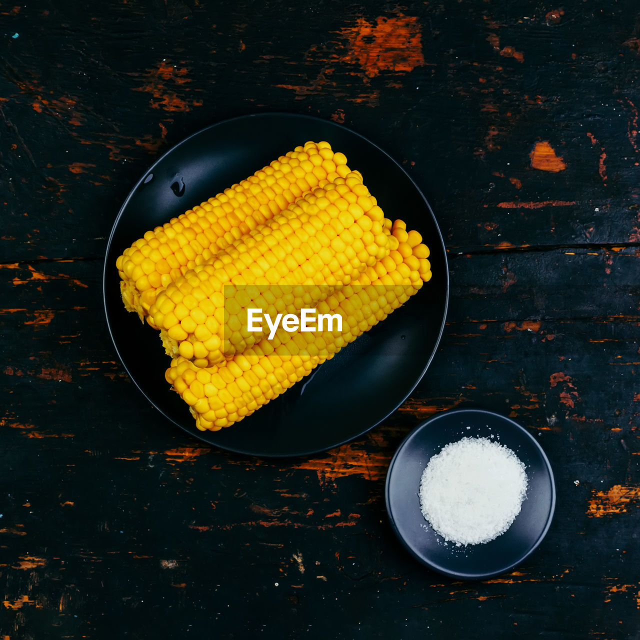 Cobs of boiled corn and salt on a black plate on a wooden vintage black table top view