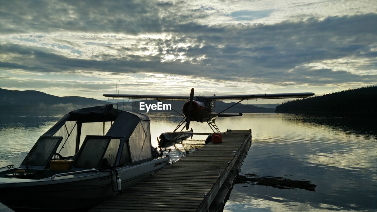 Seaplane and boat by lake against cloudy sky during sunset