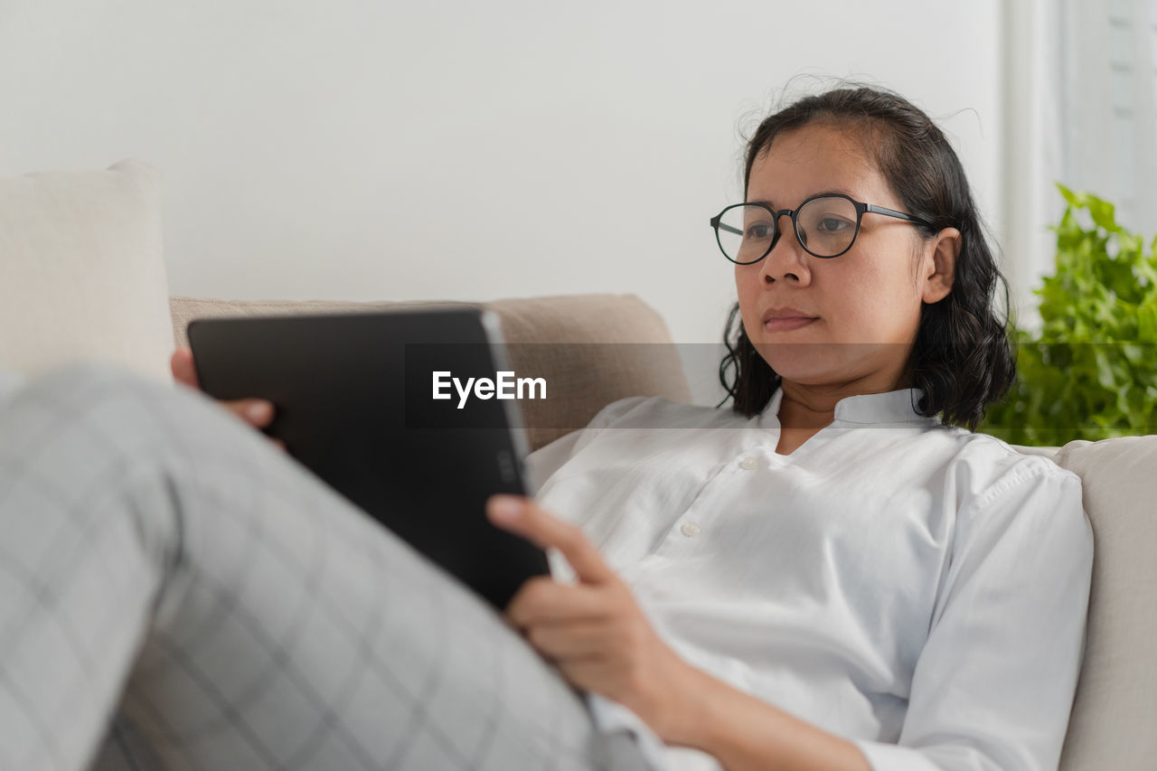 Woman using digital tablet while relaxing on sofa