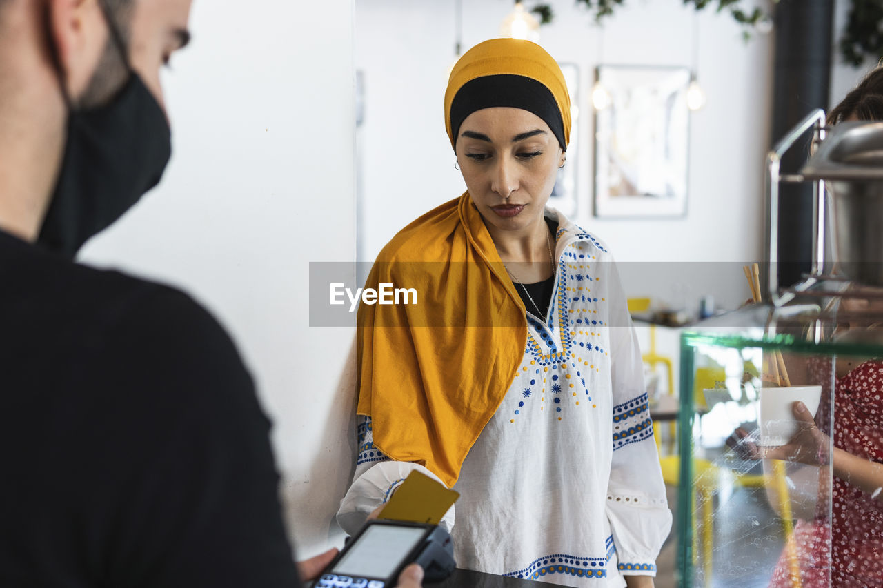 Young woman wearing headscarf paying through credit card in restaurant