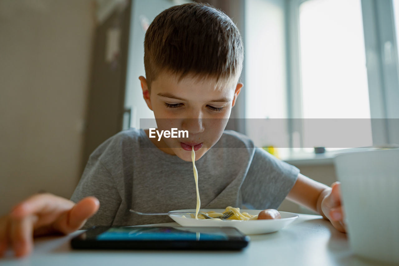 Boy, child eats pasta retraction long pasta into his mouth