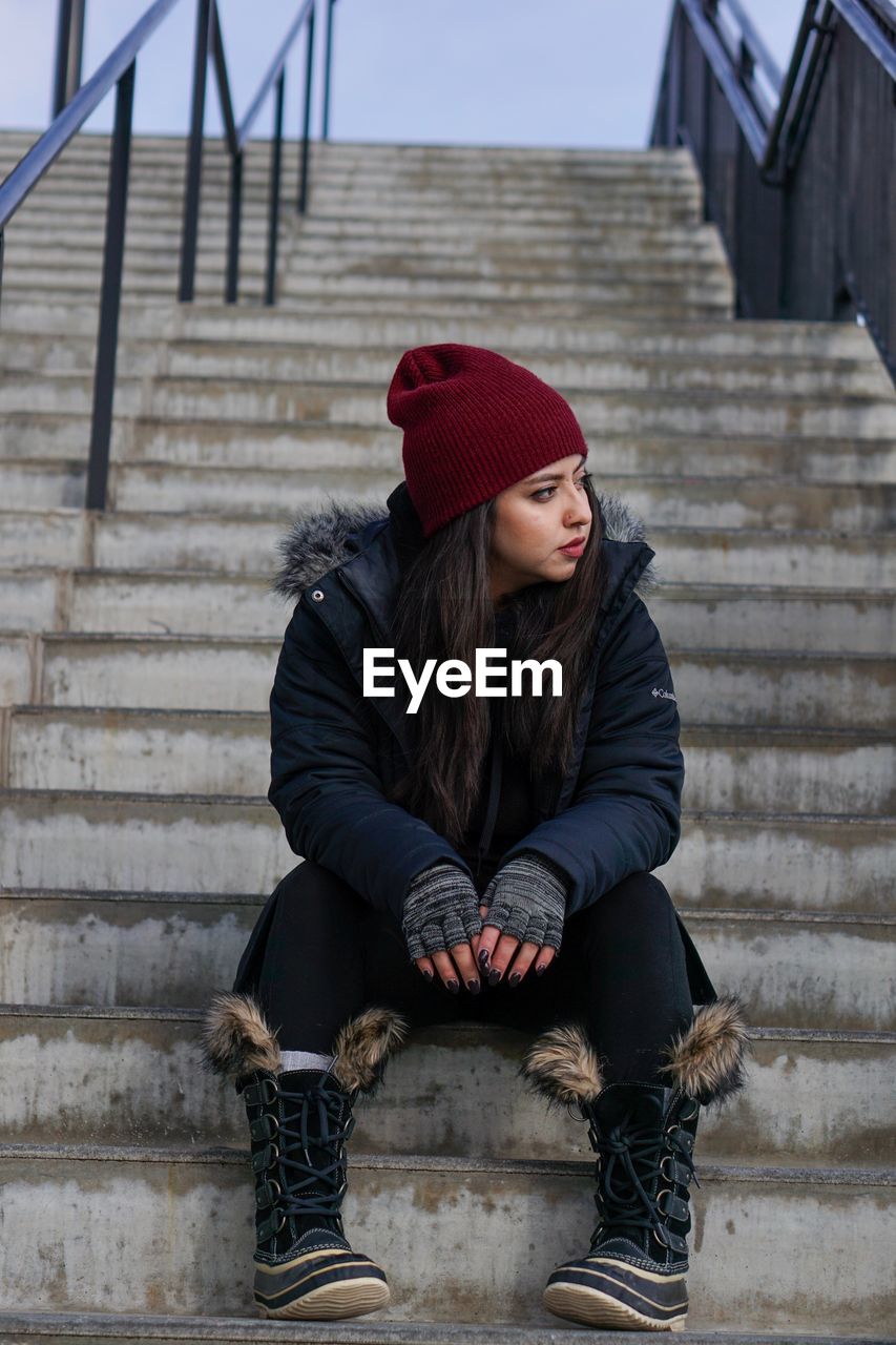 Full length of young woman looking away while sitting on staircase