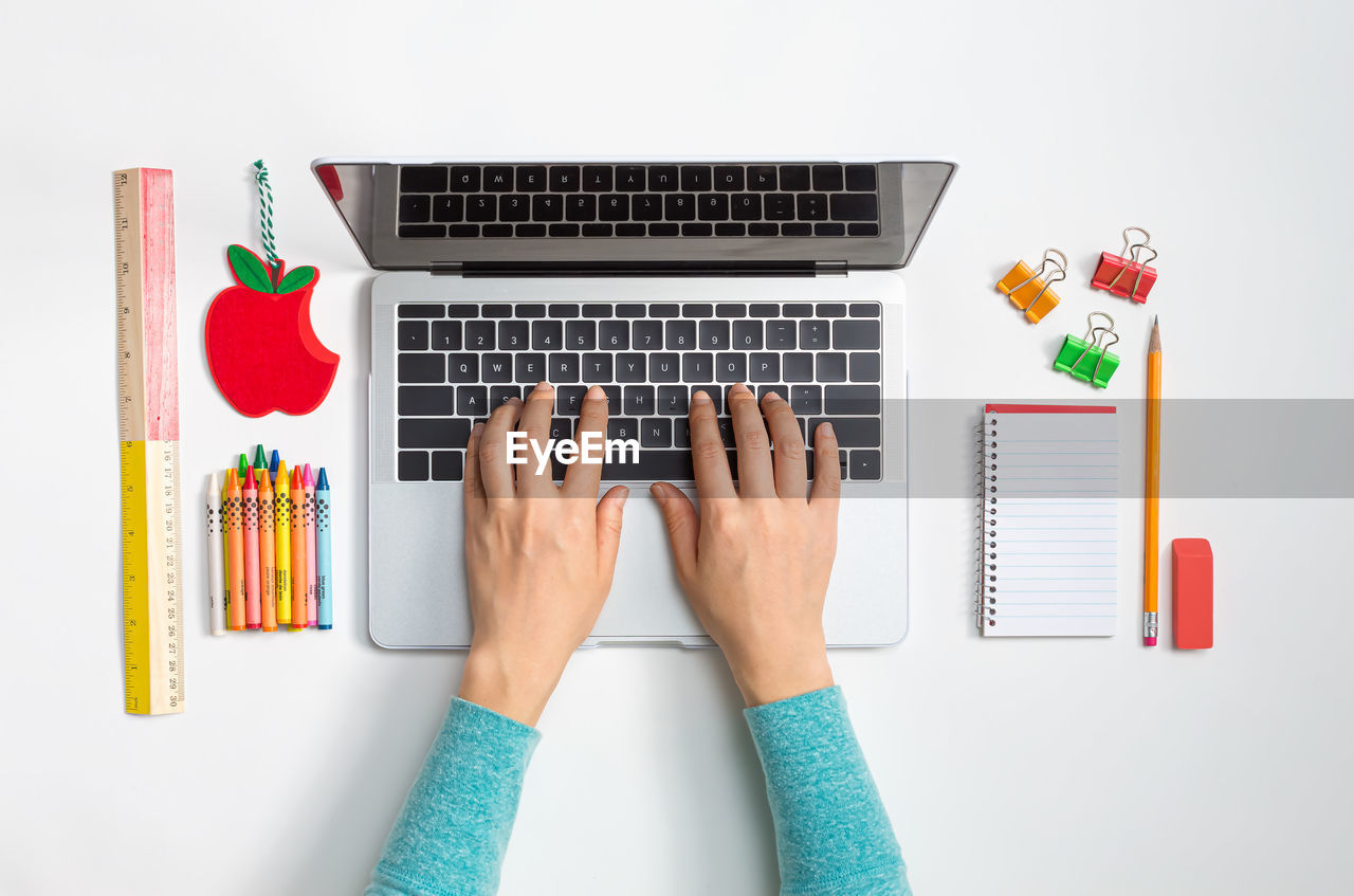 Cropped hands of woman using laptop by school supplies on white background