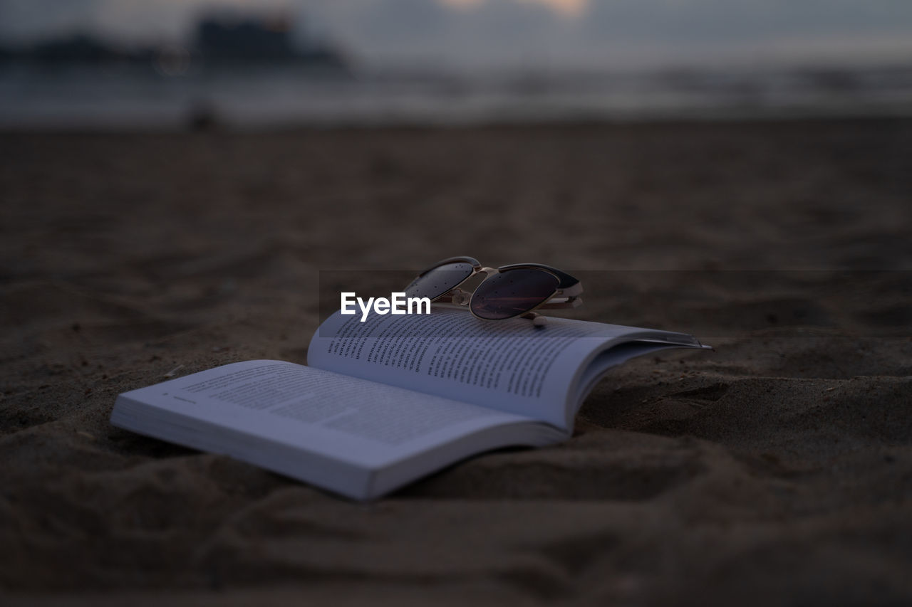 land, beach, publication, sand, book, sky, sea, nature, white, water, wave, blue, selective focus, no people, absence, outdoors, paper, tranquility, focus on foreground, footwear, emotion, flip-flops, vacation