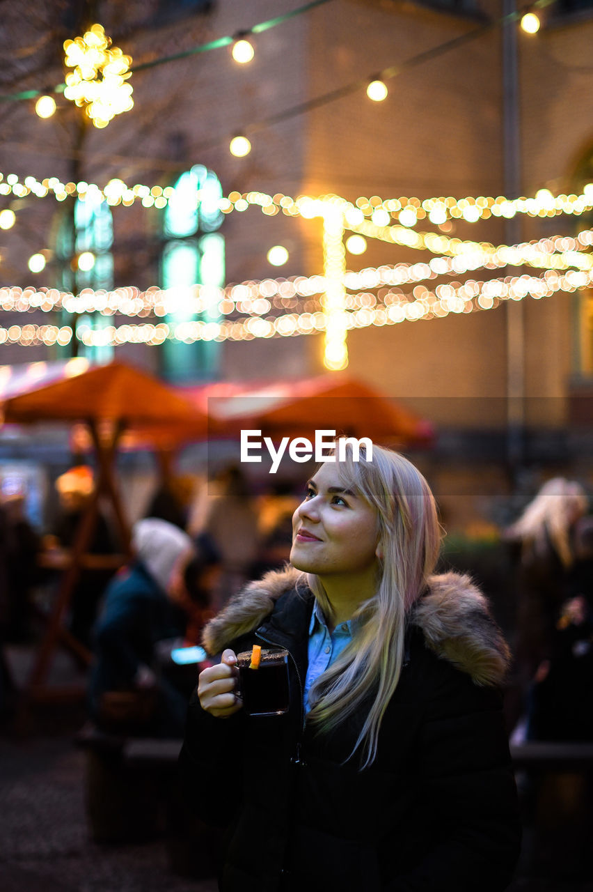 Young woman having drink at outdoor cafe in city at night