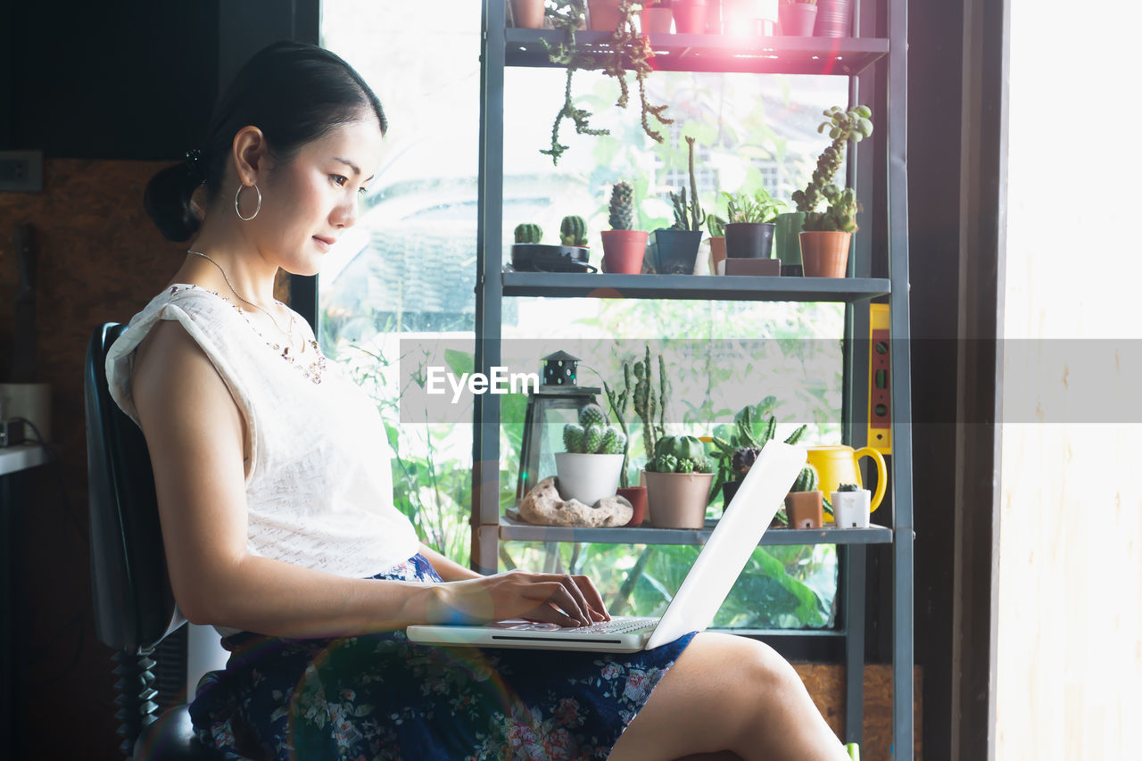 Side view of woman using laptop on chair