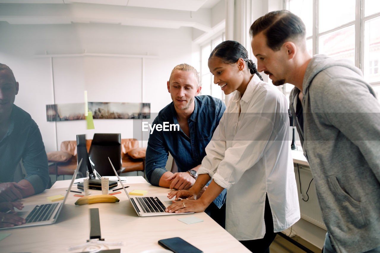 Businesswoman using laptop while discussing with male coworkers at desk in office