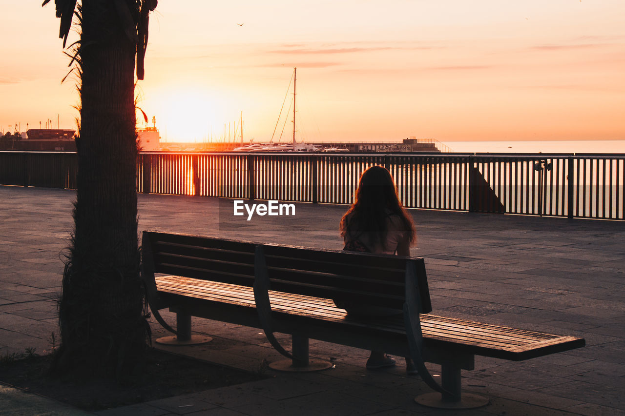 Rear view of silhouette woman sitting on bench