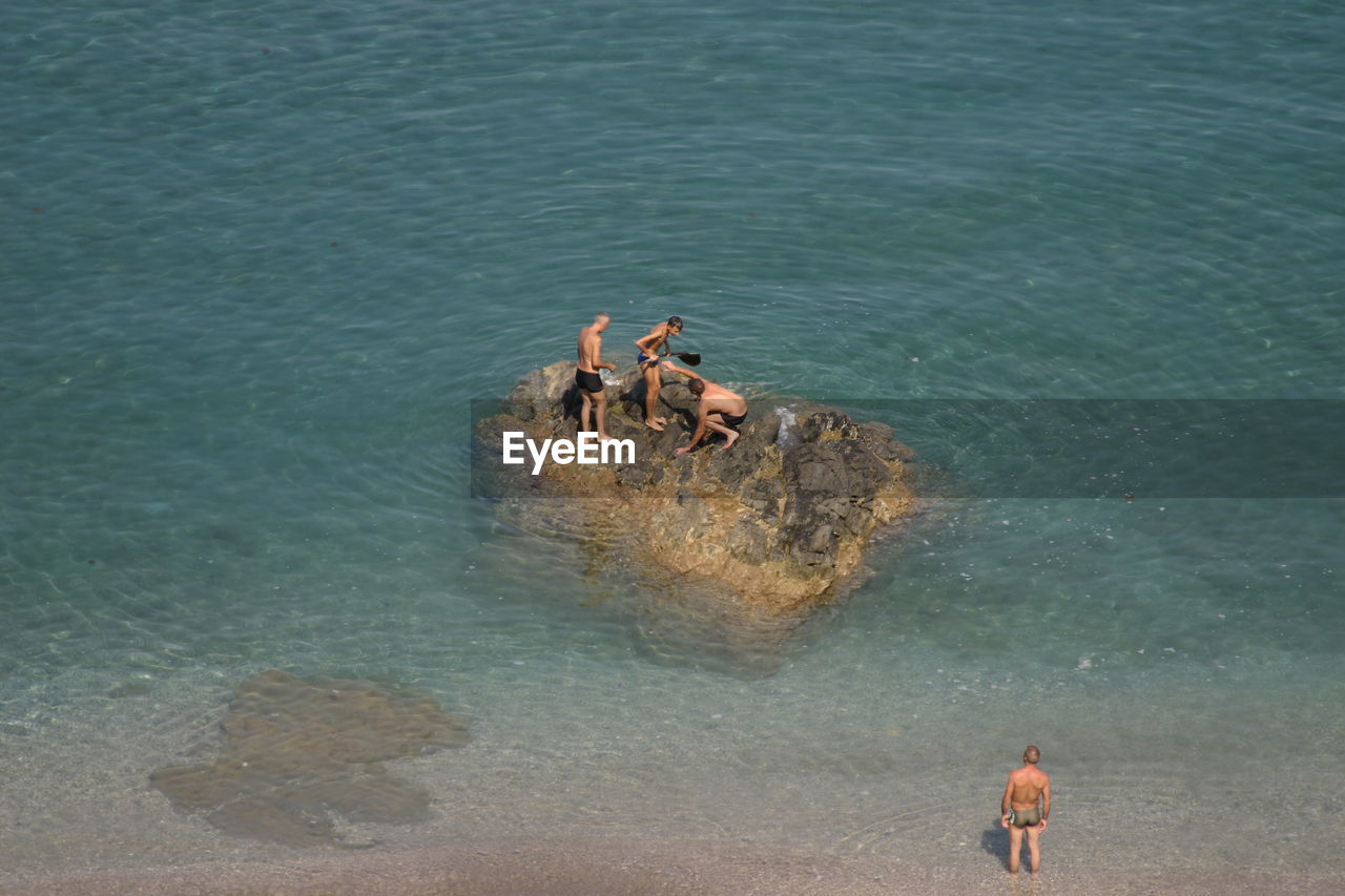 People on rock at calm blue sea