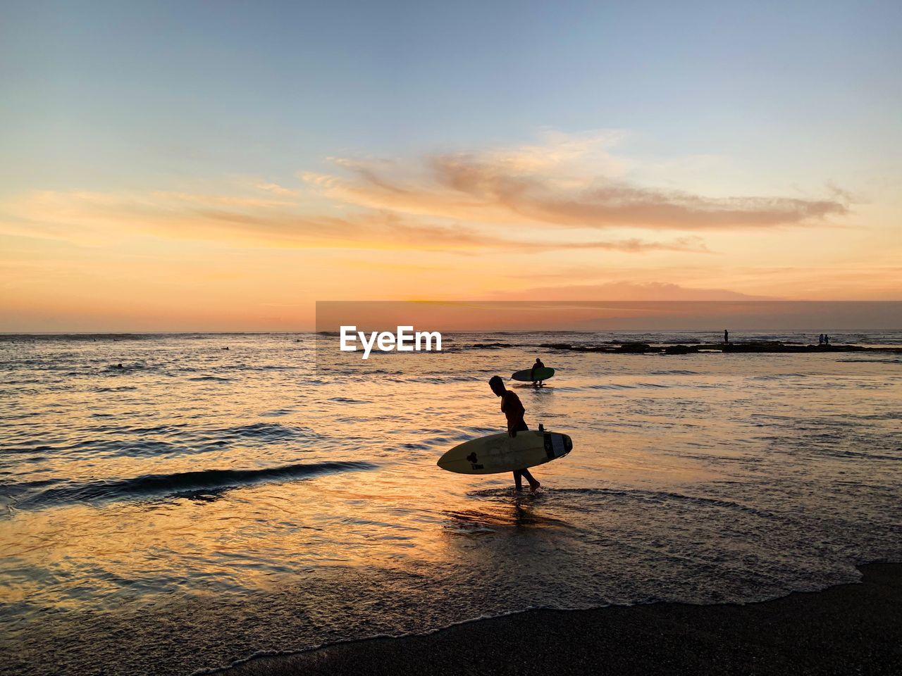 Silhouette man carrying surfboard at beach against sky during sunset