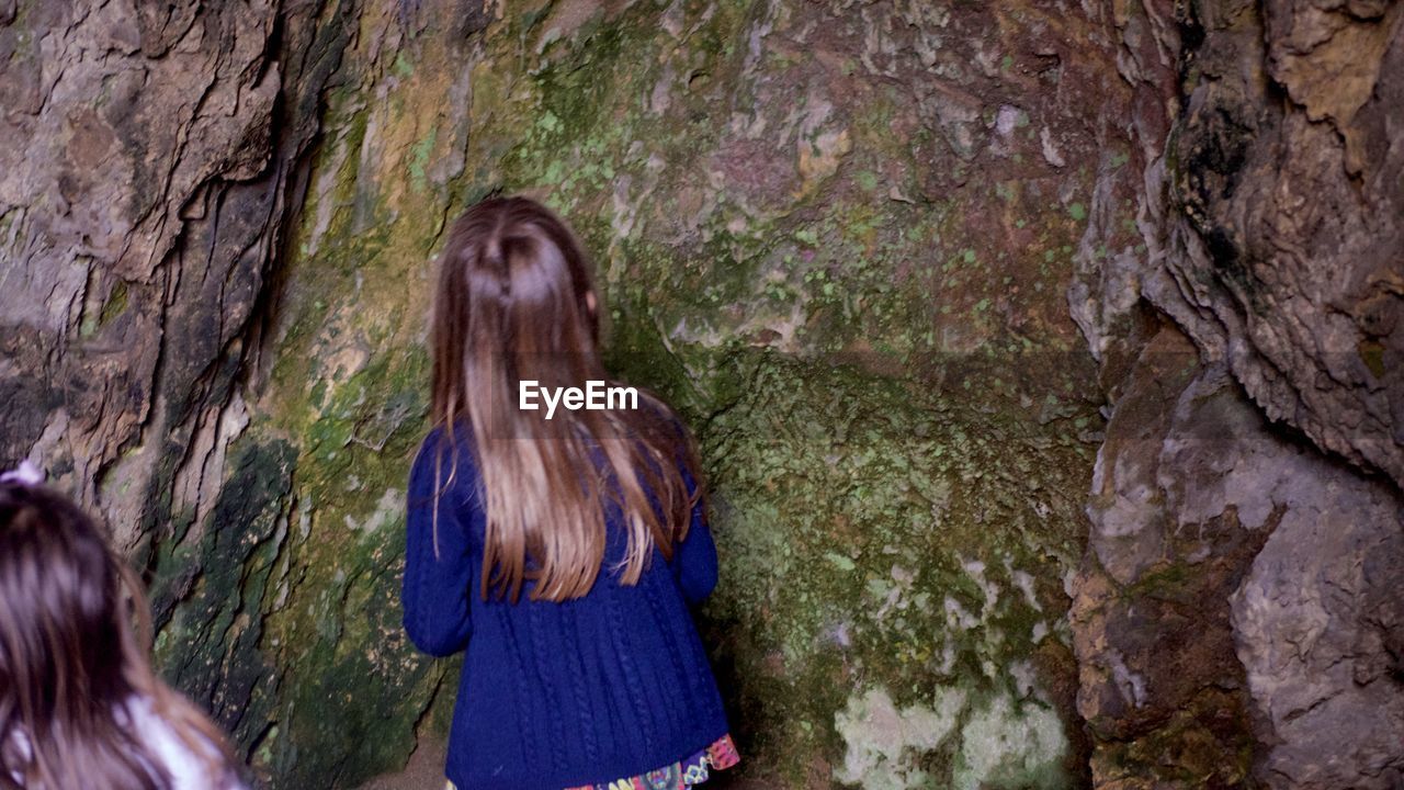 REAR VIEW OF WOMAN STANDING AGAINST ROCK