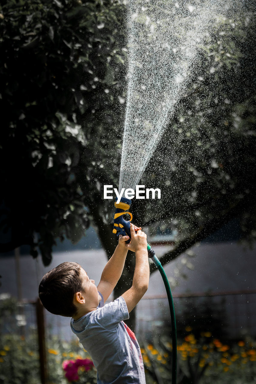 Full length of a boy holding water hose water drops childhood play