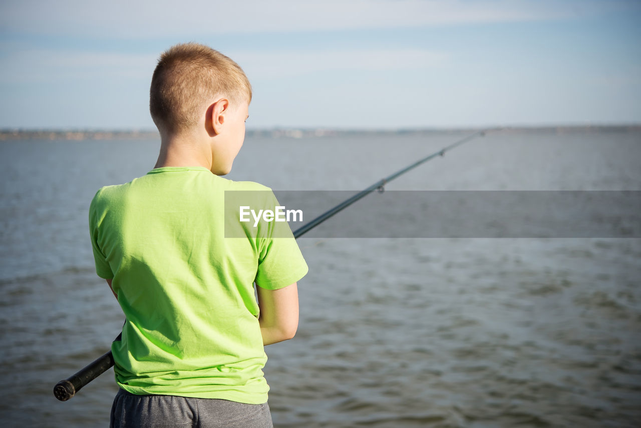 Boy fishing on a lake in the summer. view from back