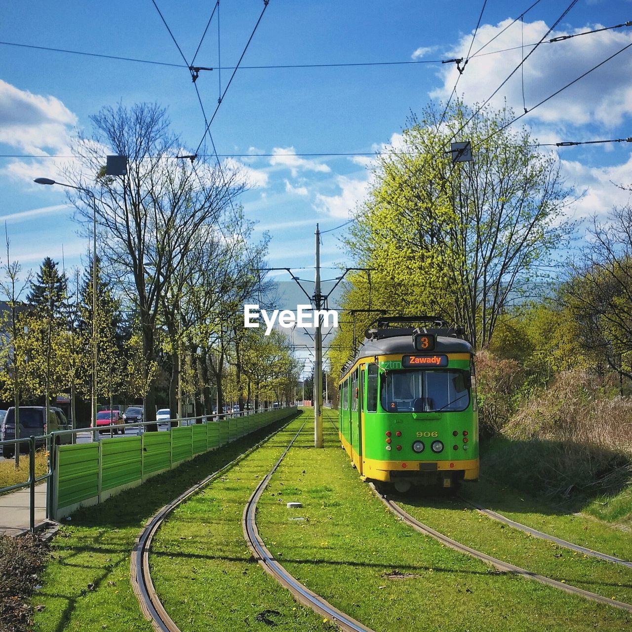 Tram on railroad track by street against cloudy sky