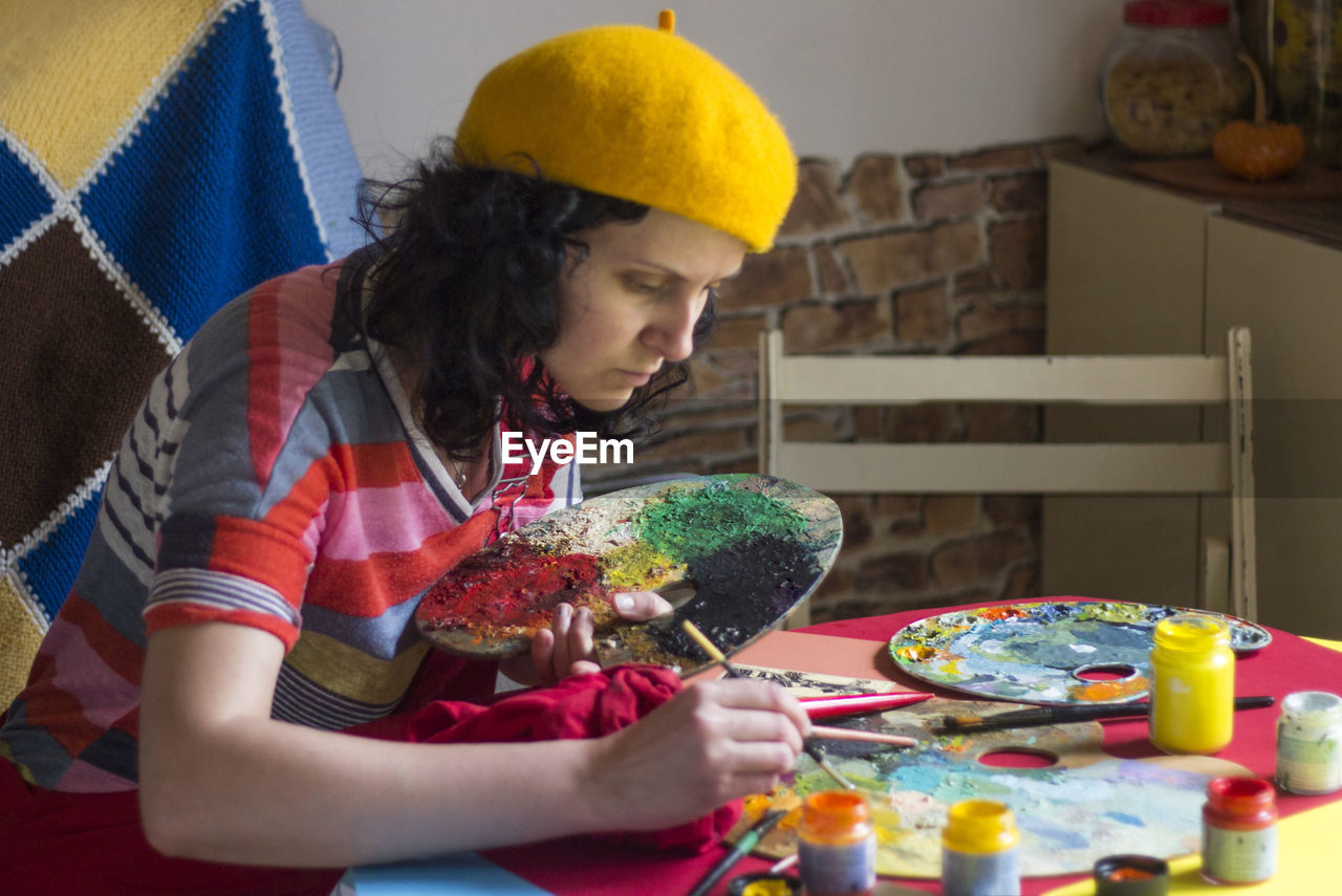 A woman with yellow hat painting on the table, colorful clothes