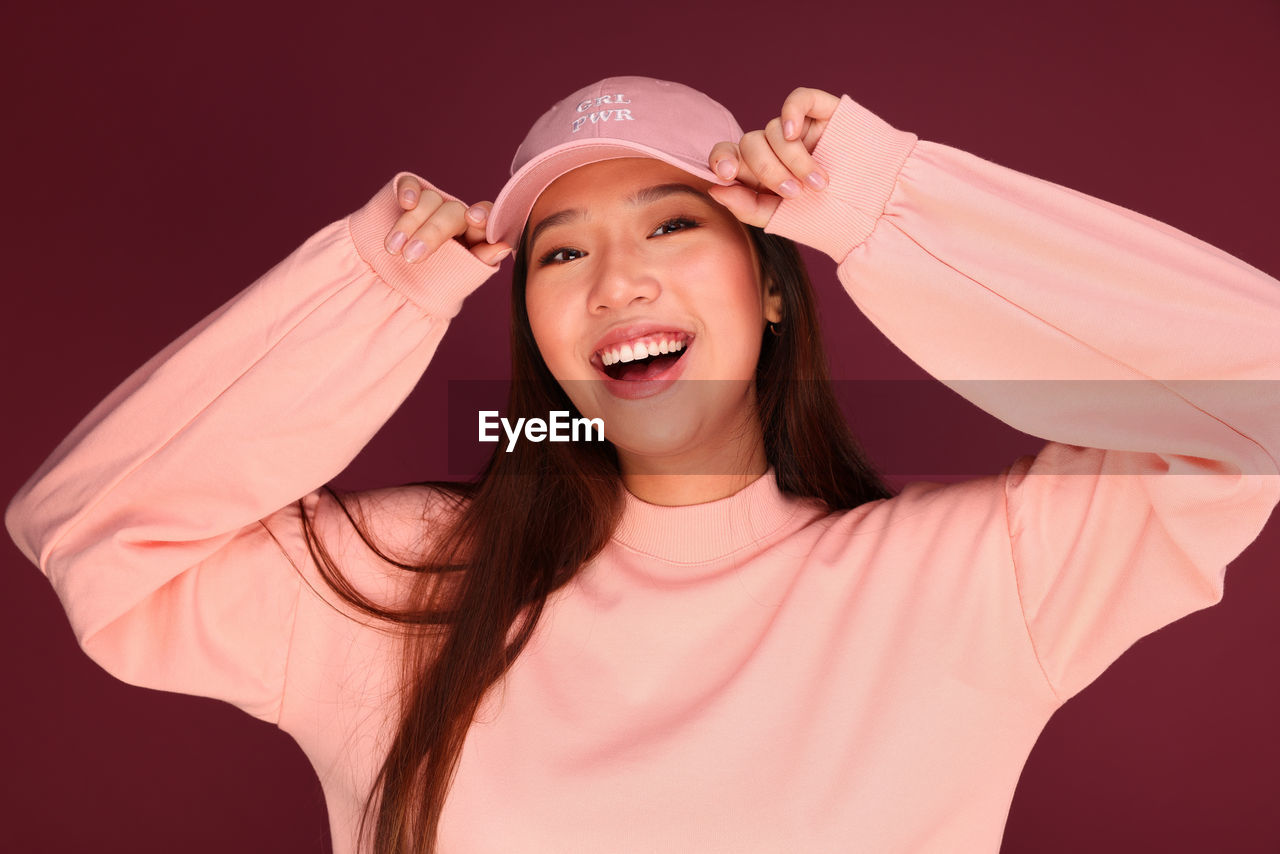 Portrait of happy young asian woman in the studio wearing pink clothes over garnet background