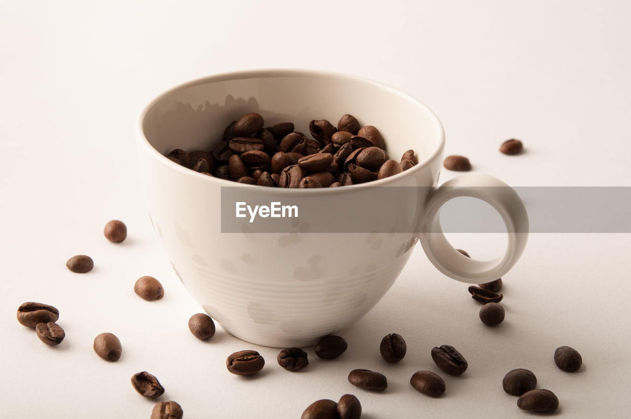 Close-up of cup with roasted coffee beans on white background
