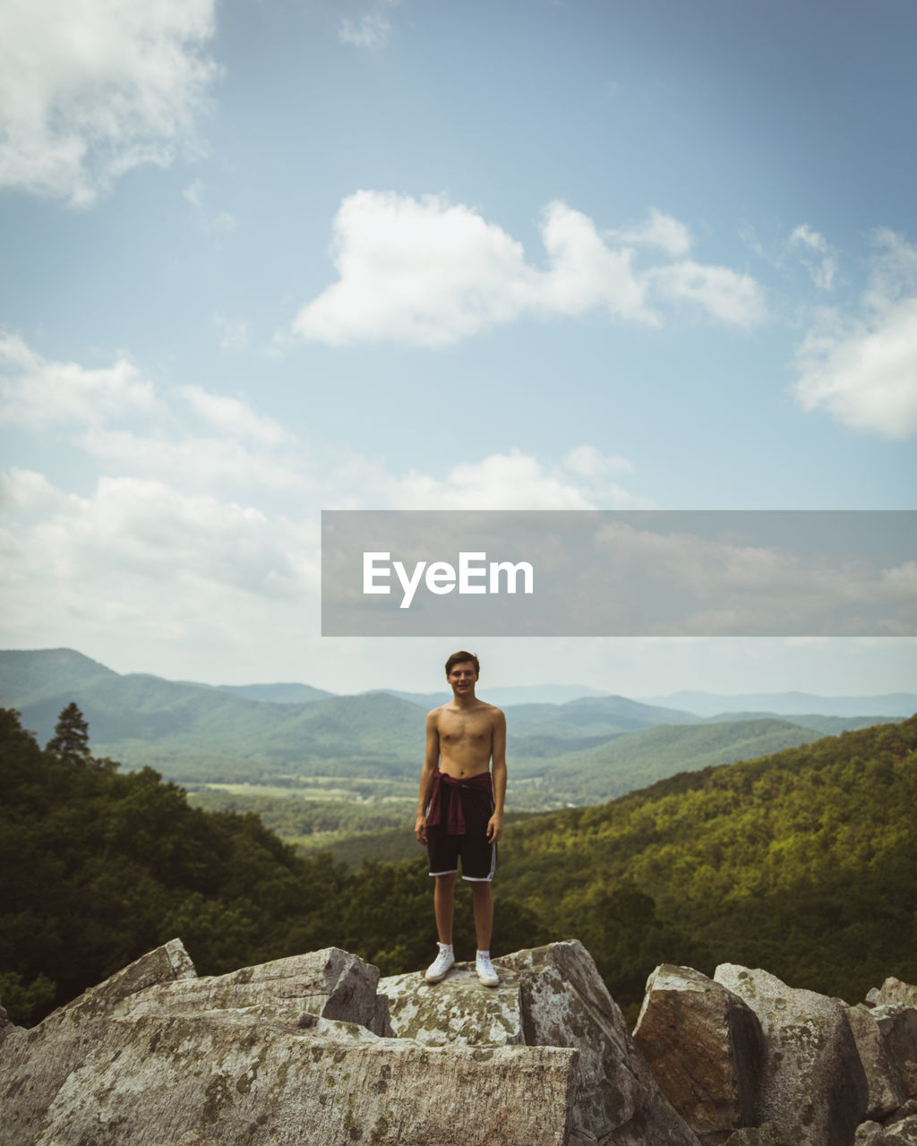 Shirtless man standing on rock against mountains