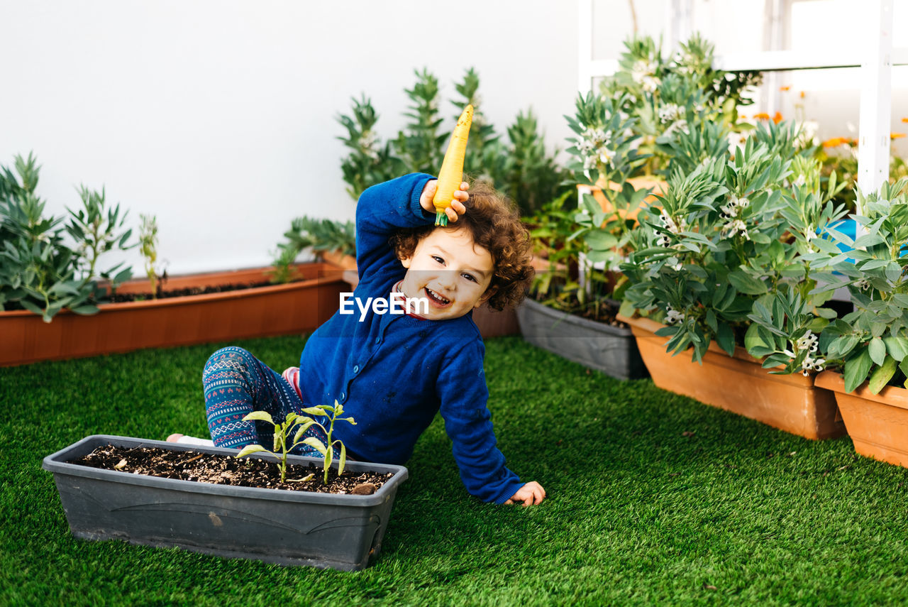 Full length portrait of boy with potted plants in yard