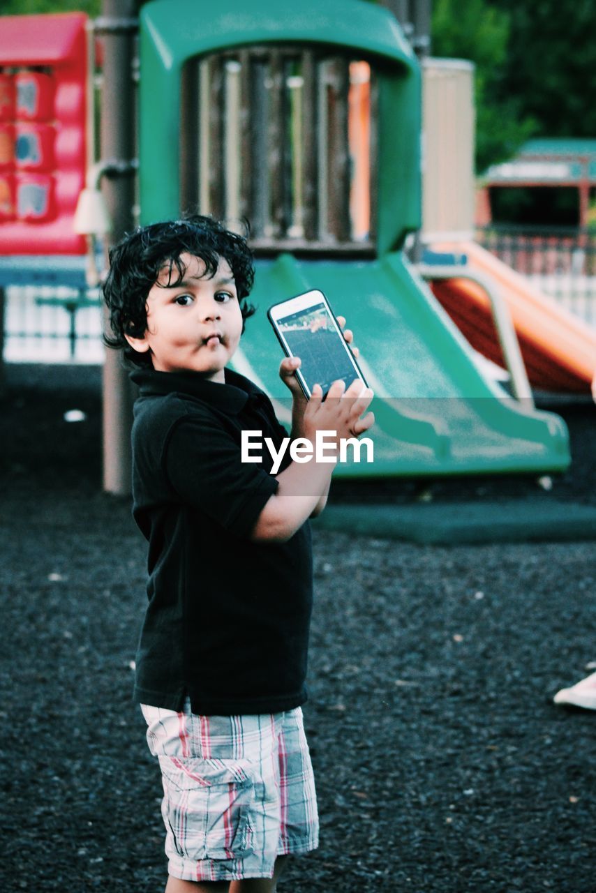 Portrait of boy holding mobile phone at playground