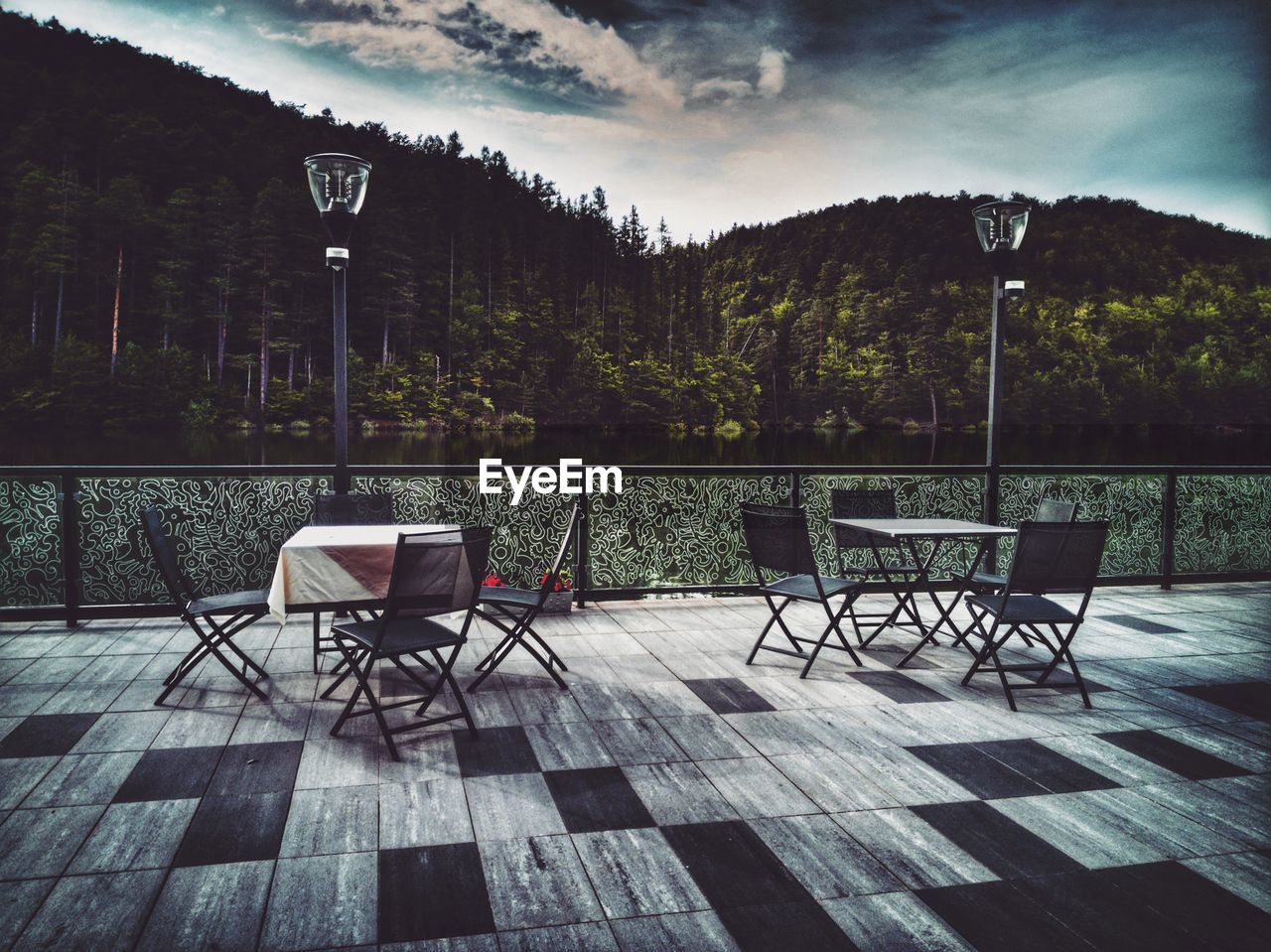 Empty chairs and table by lake against sky