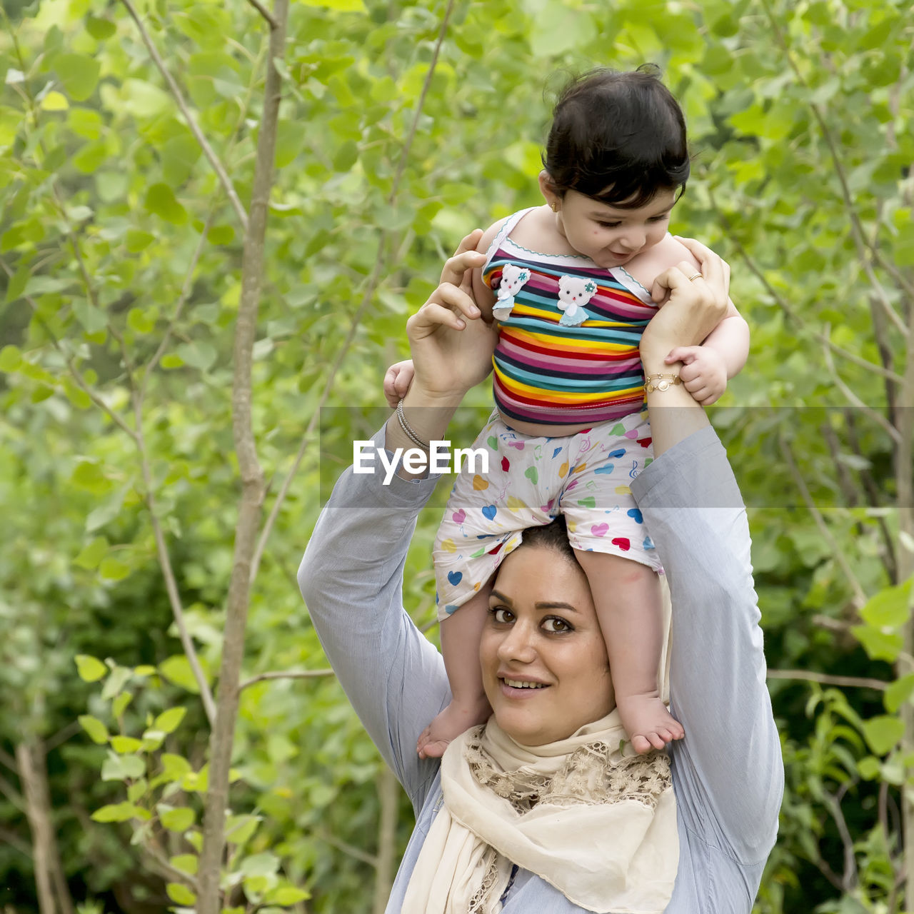 Portrait of mother carrying daughter on head against plants