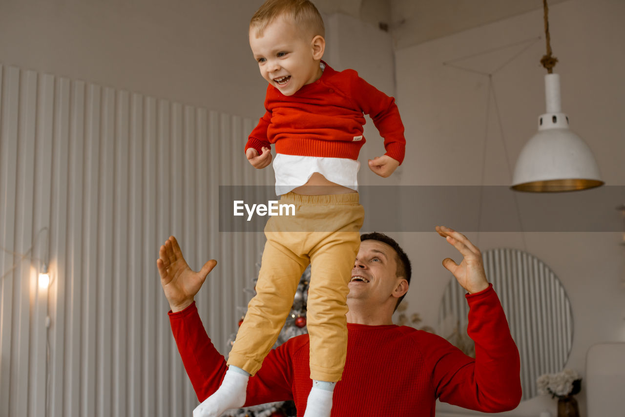 Cheerful happy father throwing up his adorable laughing son in bright room with christmas interior