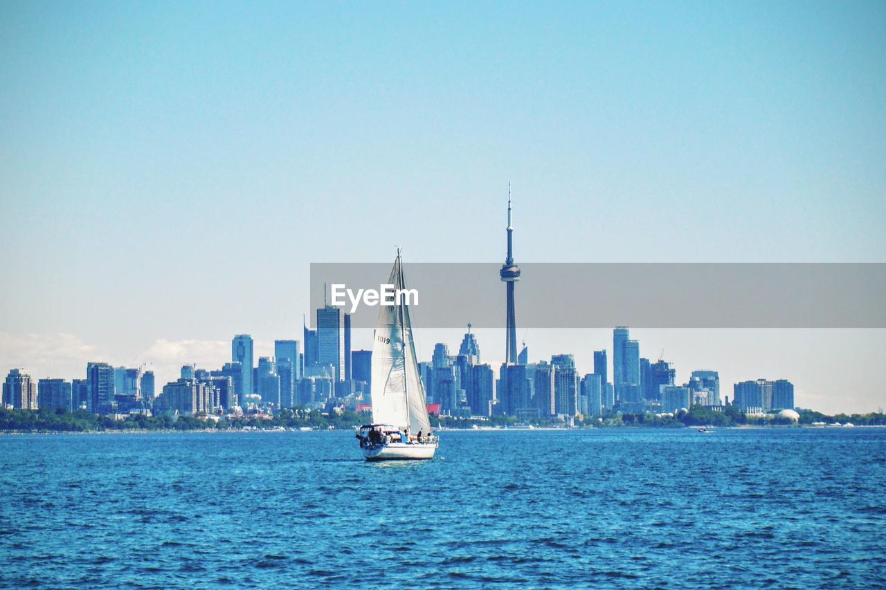Sailboat sailing in sea by cn tower and city against sky