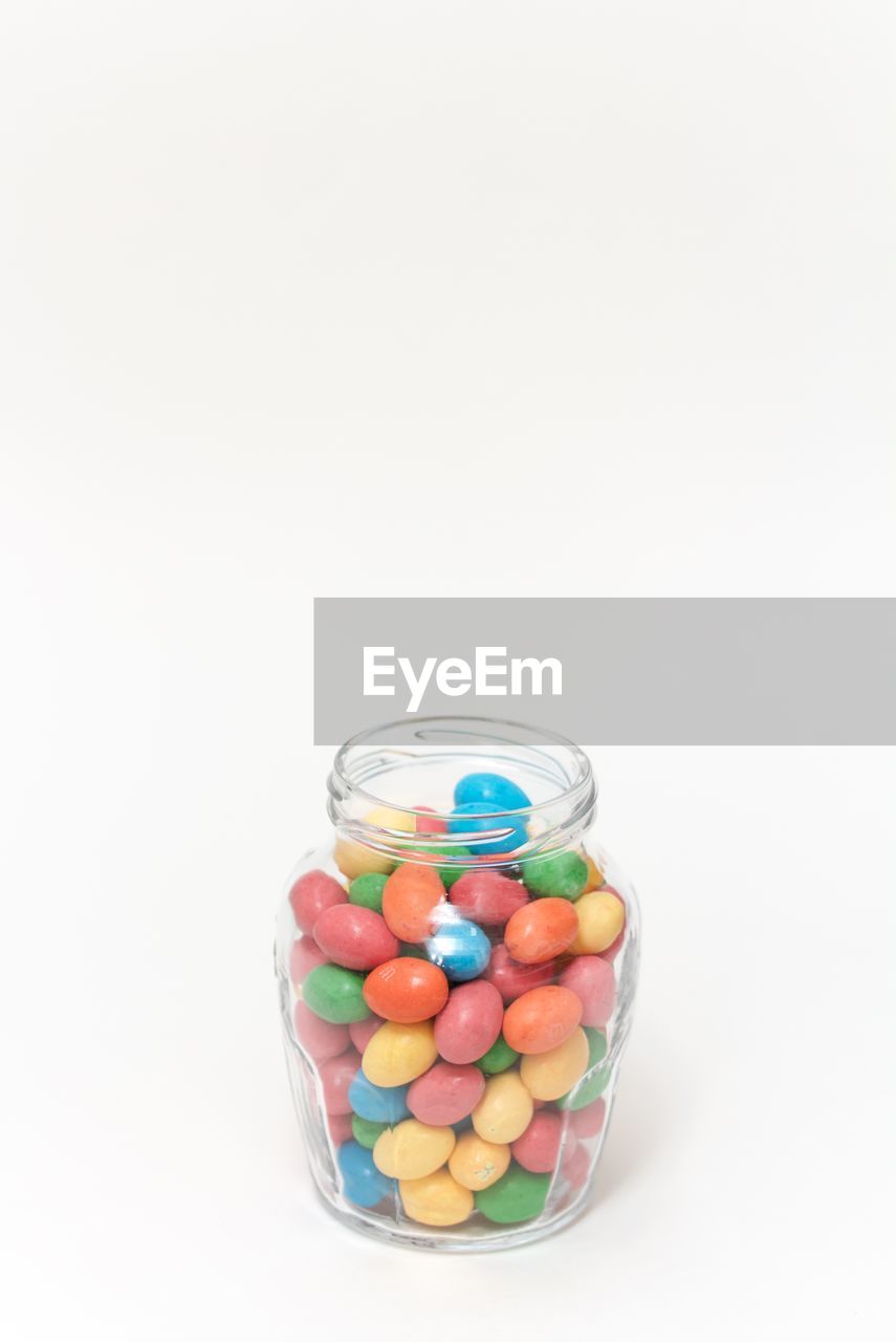 Close-up of colorful candies in jar against white background