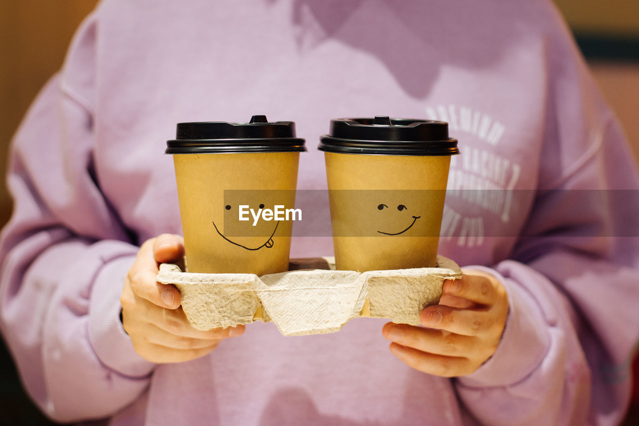 Two craft coffee cups with painted smiley in hands