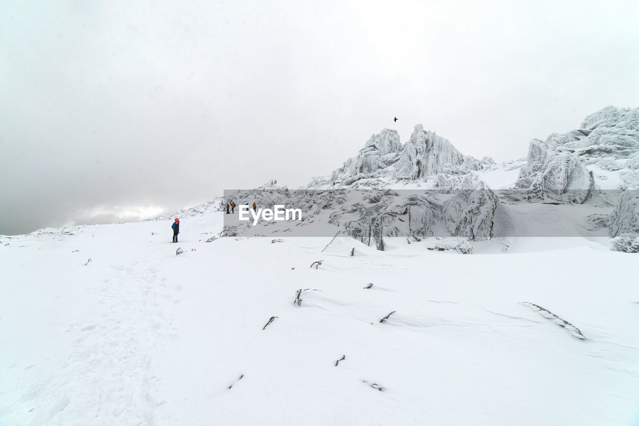 People hiking on snowcapped mountain against sky