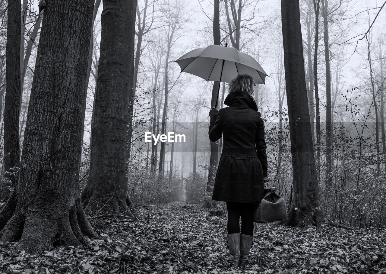 FULL LENGTH OF WOMAN STANDING BY TREE TRUNK IN RAIN