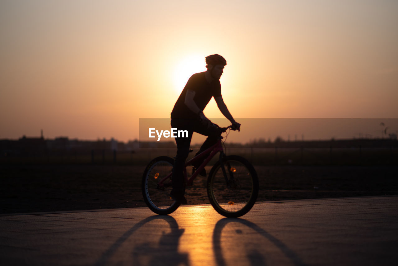 Full length of man cycling on road against sky during sunset