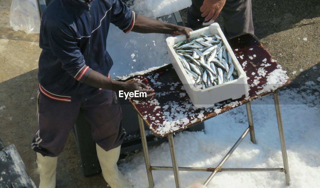 High angle view of fisherman with fish in box by ice crushing machine at harbor