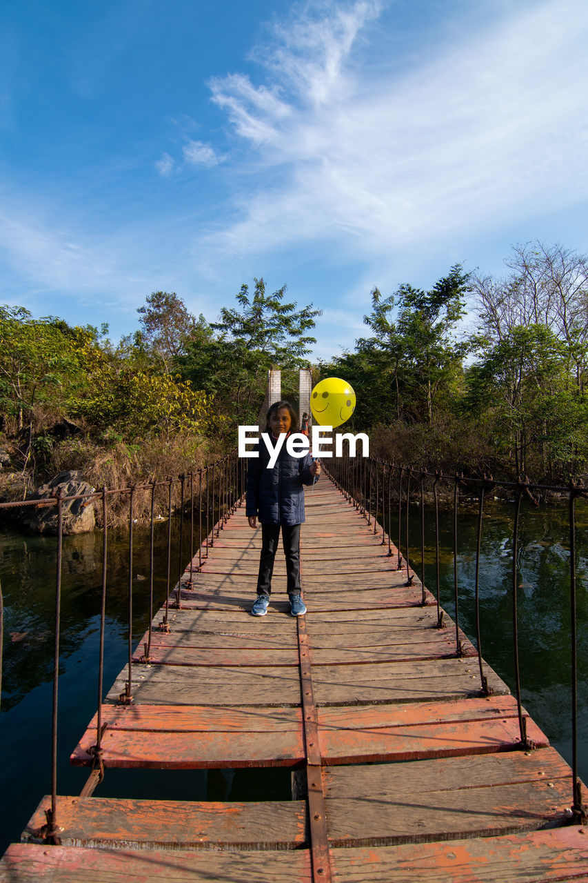 full length, one person, sky, nature, adult, tree, reflection, men, sports, walkway, cloud, plant, water, architecture, leisure activity, outdoors, day, wood, standing, bridge, lifestyles, footpath, vacation, railing